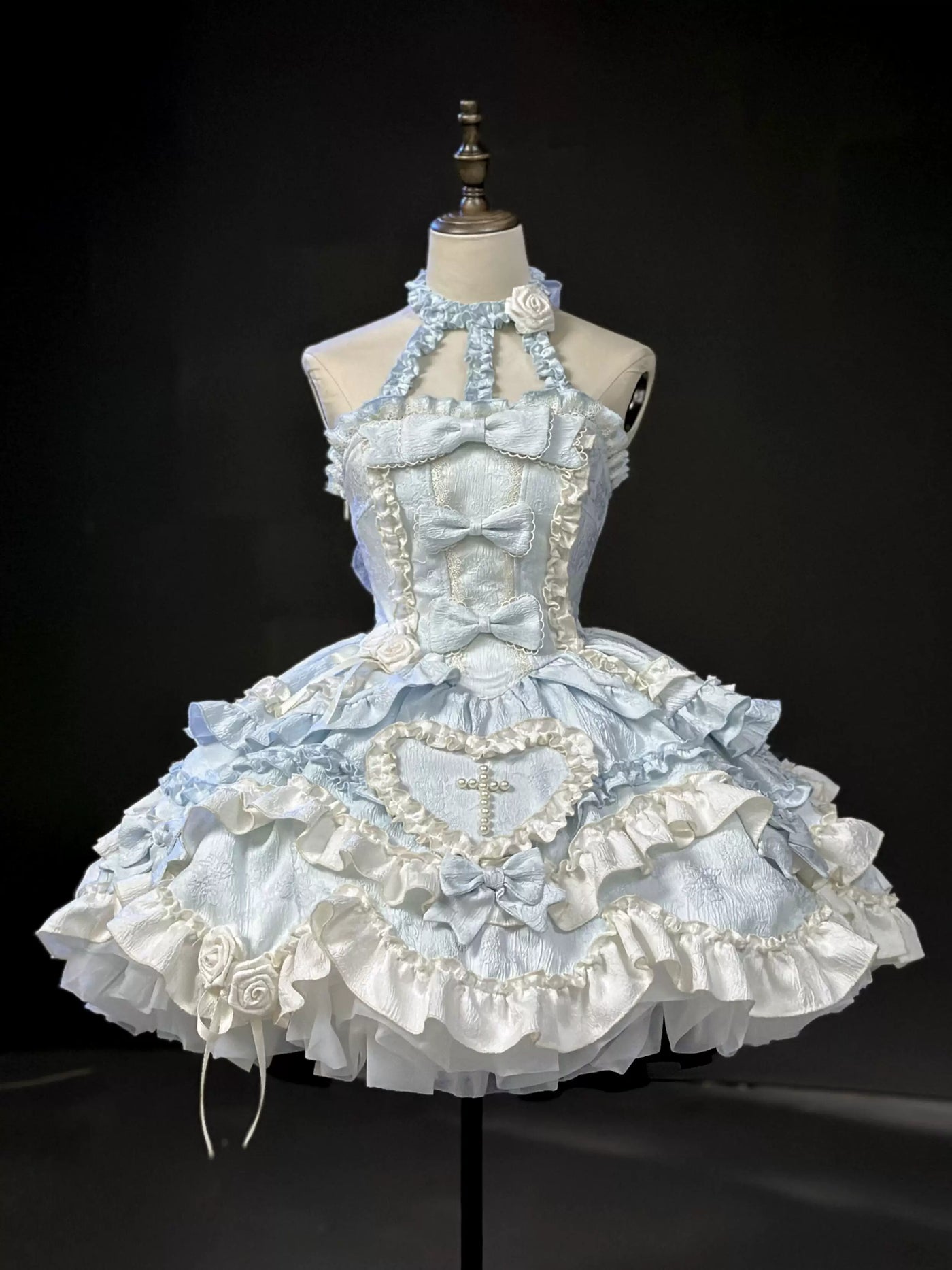 Blue-and-white JSK dress displayed on a dress form with layered bows, ruffles, roses, and a pearl cross.