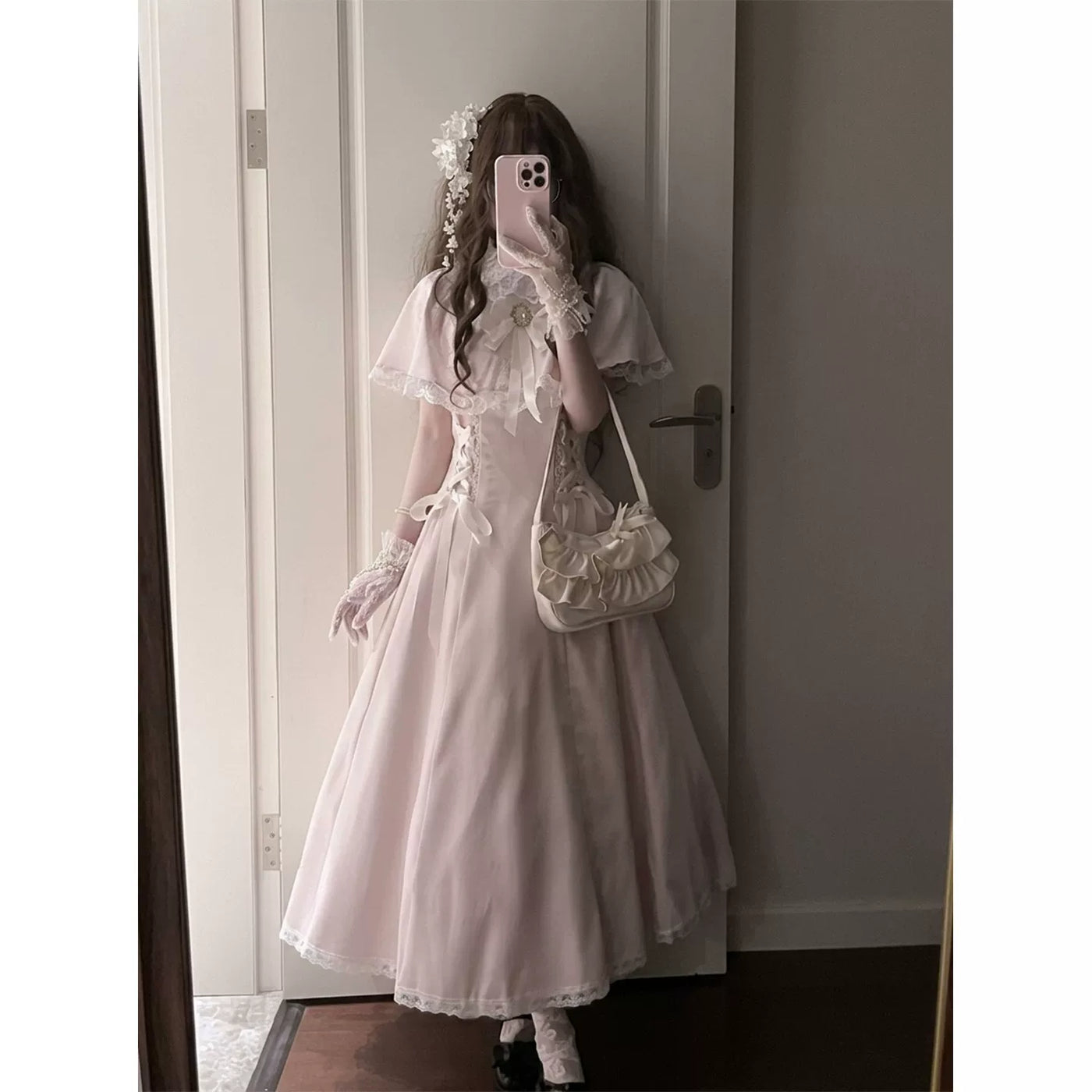 Model wearing a pale pink long one-piece dress with lace-trimmed cape sleeves.