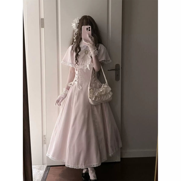 Model wearing a pale pink long one-piece dress with lace-trimmed cape sleeves.
