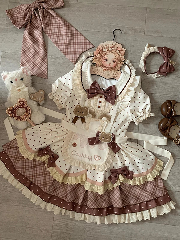 Flat-lay cream and brown bear-themed OP dress set with apron, bows and plaid skirt.