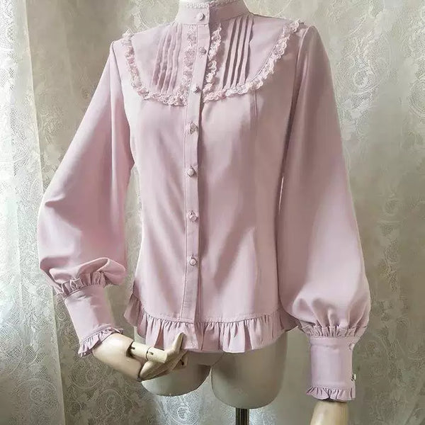 White and black long-sleeve Lolita blouses with stand collars, pleated fronts and ruffled hems on mannequins.