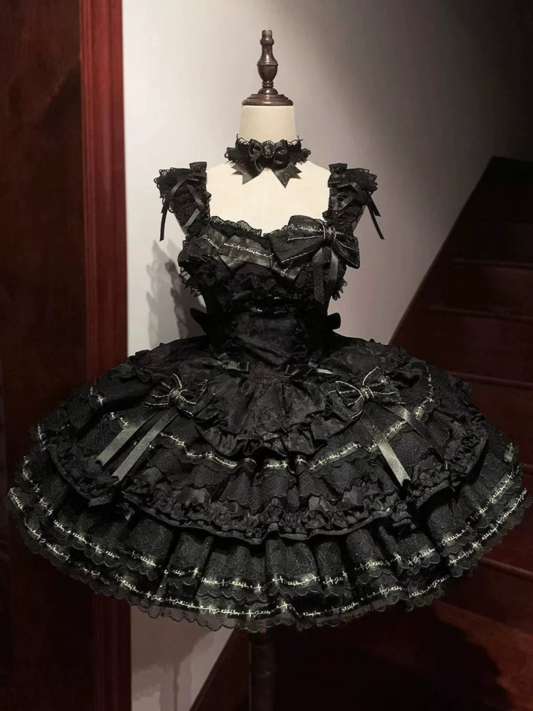 Black layered one-piece dress with a large train, bows, and gold-toned detailing displayed on a mannequin