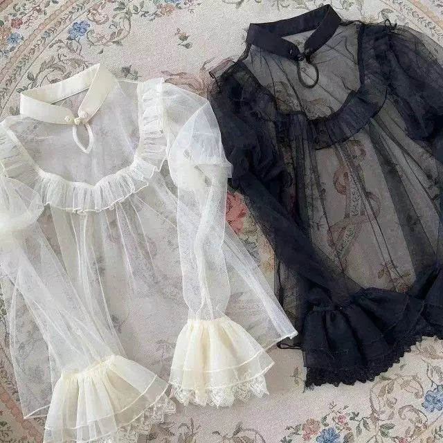 Ecru and black long-sleeve blouses with ruffled mesh panels and frog buttons laid flat