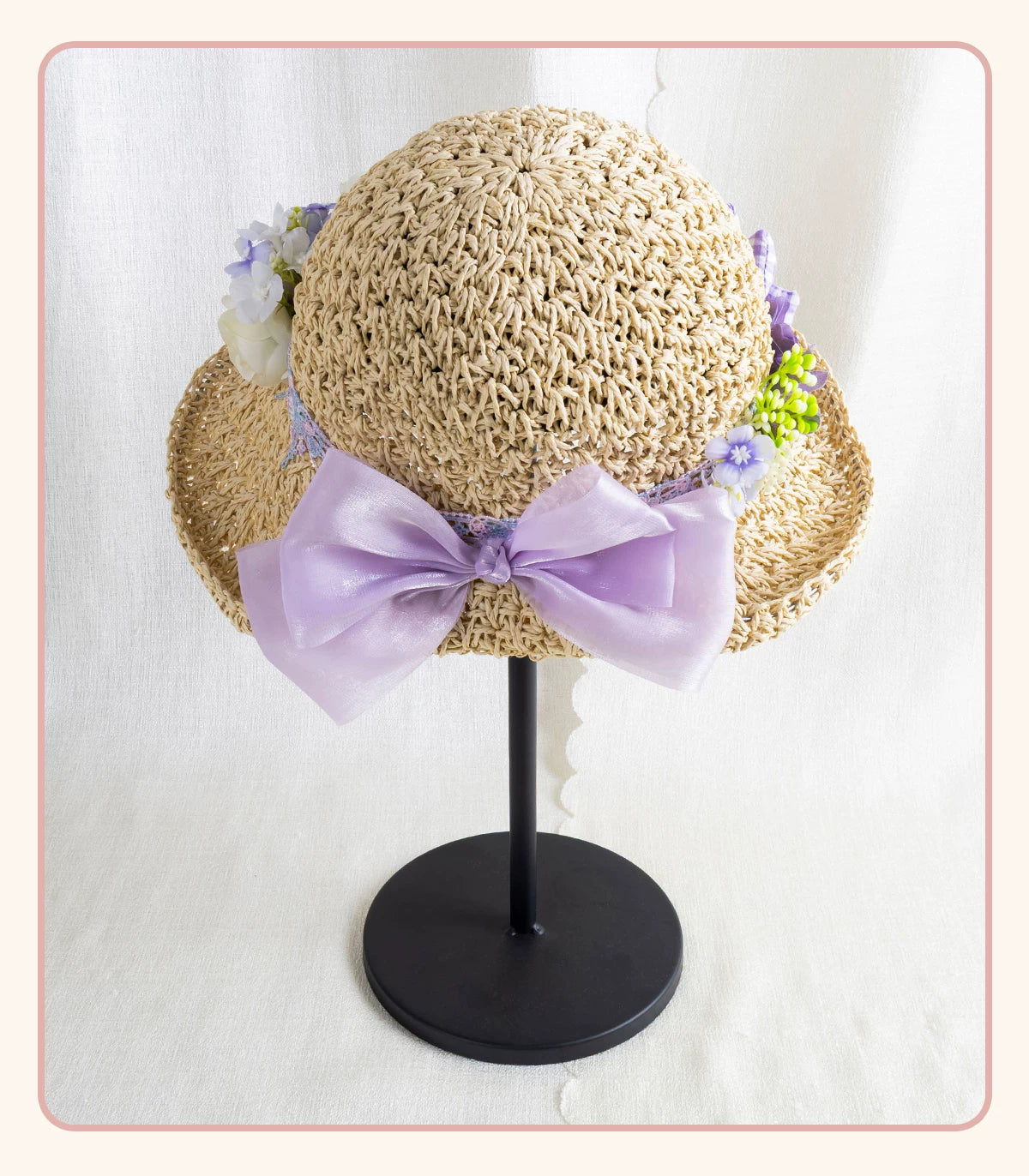 Textured woven straw hat with lavender bow and floral trim displayed on a black stand.