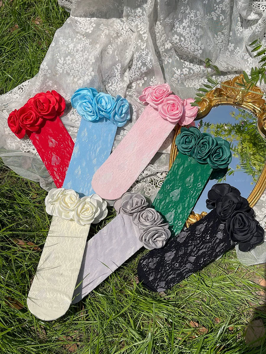Seven colourways of slouchy lace mid-calf socks with clustered camellia flower cuffs arranged on lace fabric.