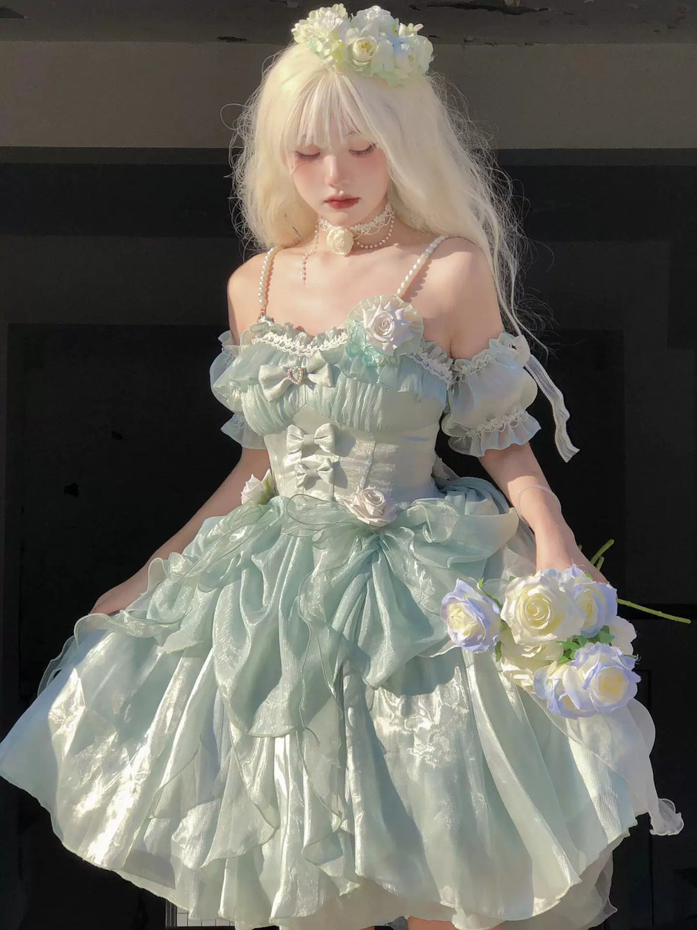 Model wearing a pale green JSK with layered ruffles, bows and floral appliqués.