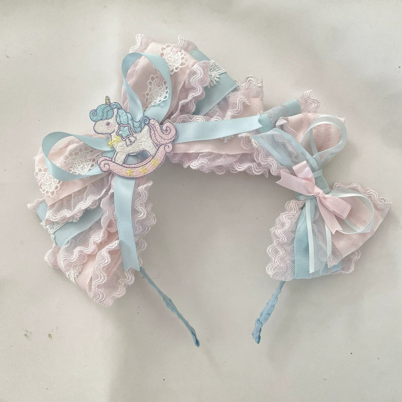 Pastel pink-and-blue lace headband with a rocking-horse motif and ribbon ties
