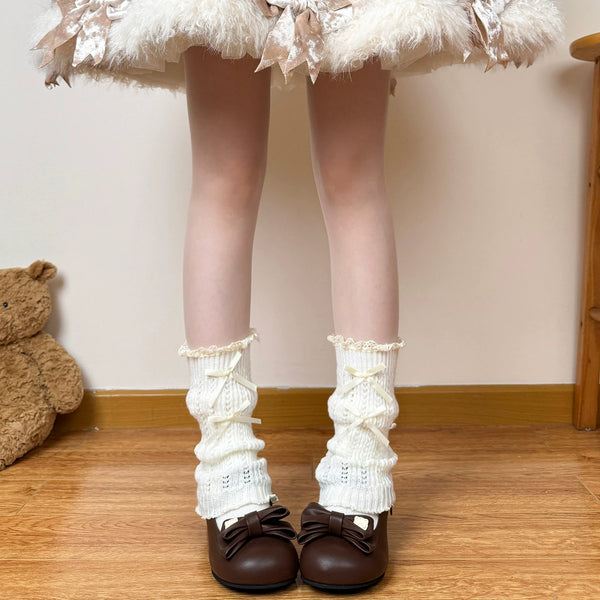Off-white slouchy leg warmers with ribbon bows and lace cuffs styled with brown shoes.
