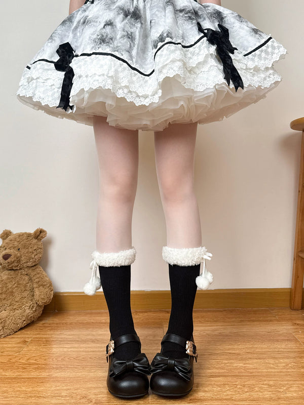 Model wearing white plush mid-calf scrunch socks with dangling pom-pom ties and brown Mary Jane shoes.