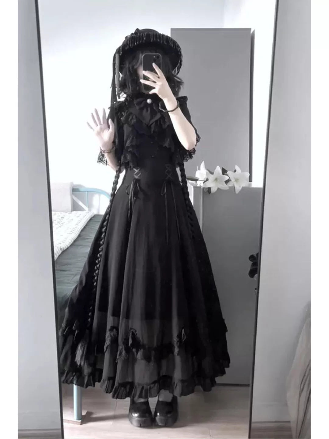Mirror image of a model wearing a black long dress with a lace cape overlay and ruffled hem.