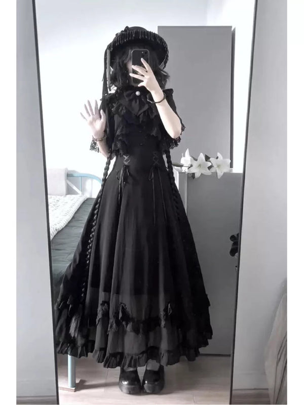 Mirror image of a model wearing a black long dress with a lace cape overlay and ruffled hem.