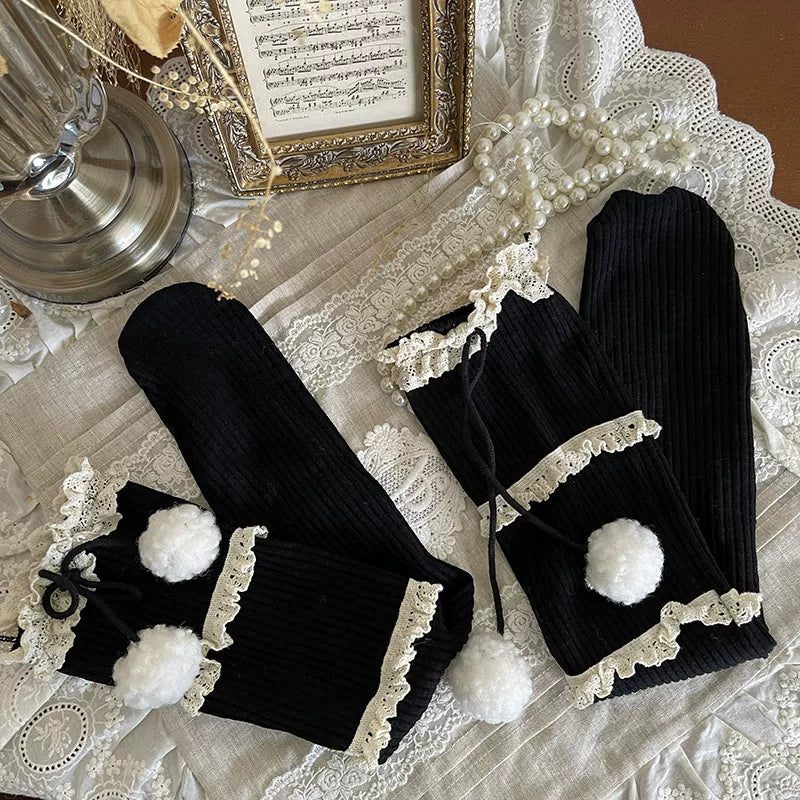 Black ribbed mid-calf socks with three lace bands, ribbon ties, and plush pom-poms worn with a Lolita coordinate.