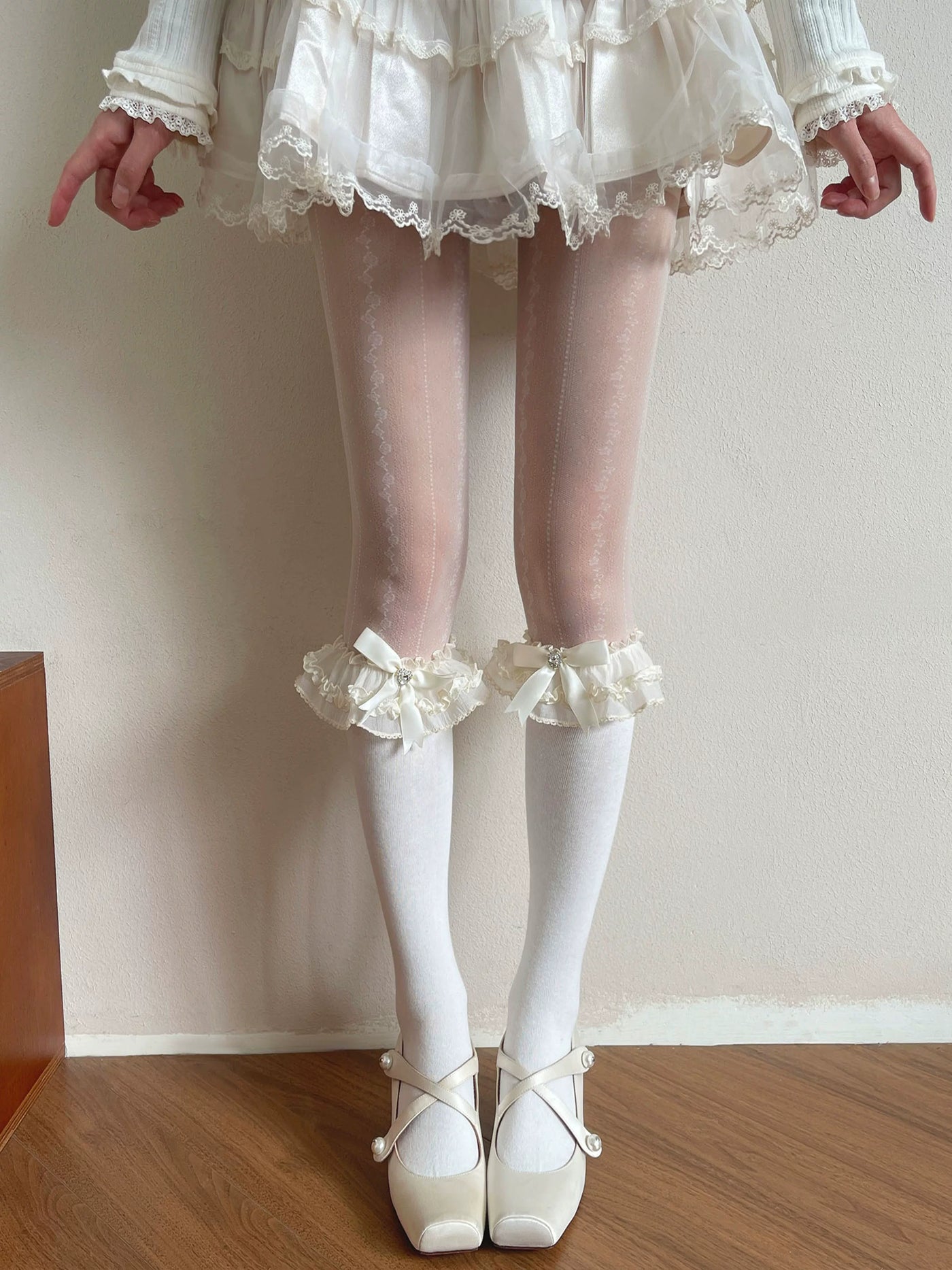 Pale hosiery styled with lace cuffs and bows under a light Lolita dress