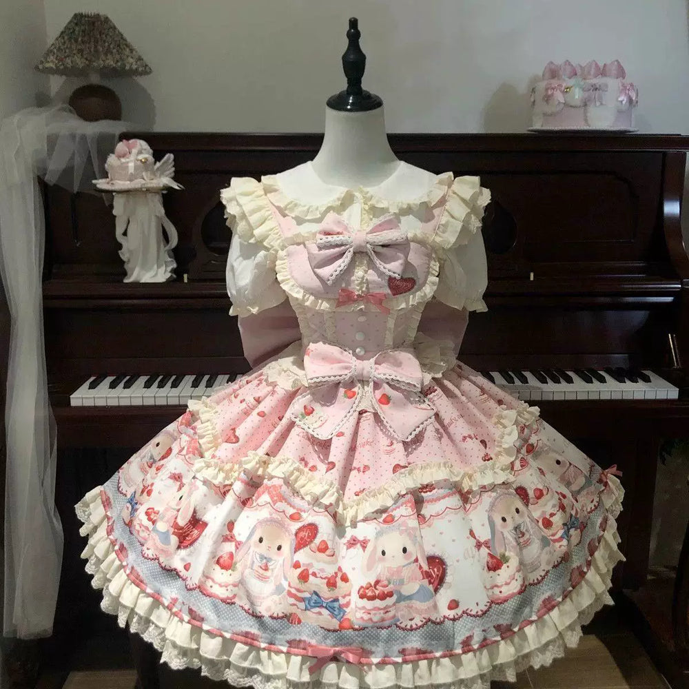 Pink and blue rabbit-and-cake print JSK dresses with cream ruffles and oversized bows displayed on mannequins.