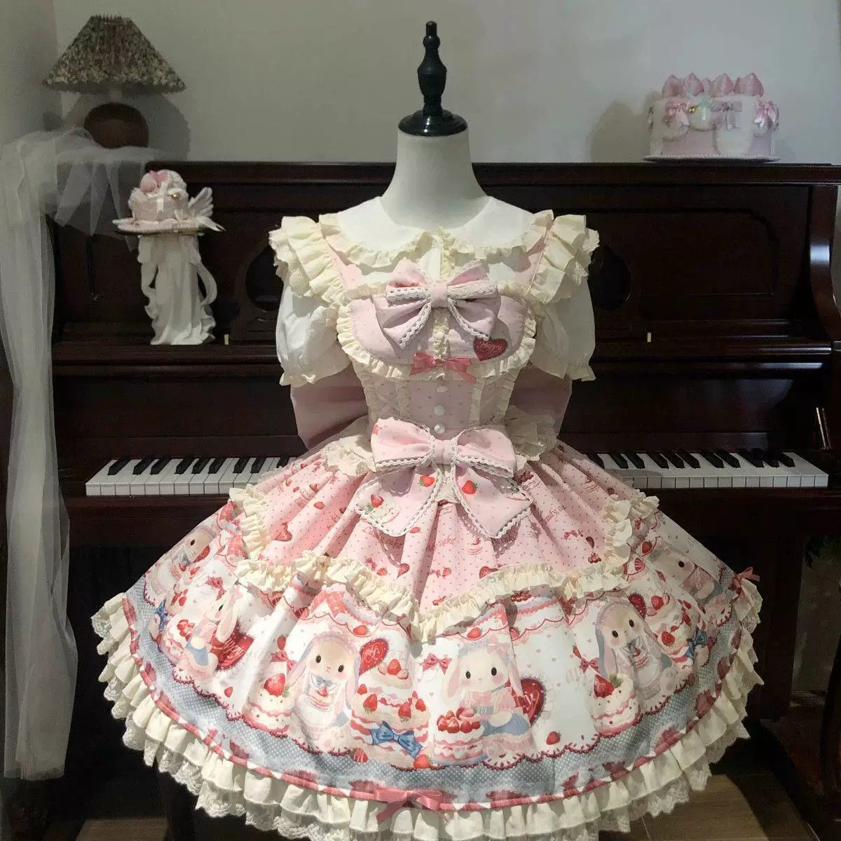 Pink and blue rabbit-and-cake print JSK dresses with cream ruffles and oversized bows displayed on mannequins.