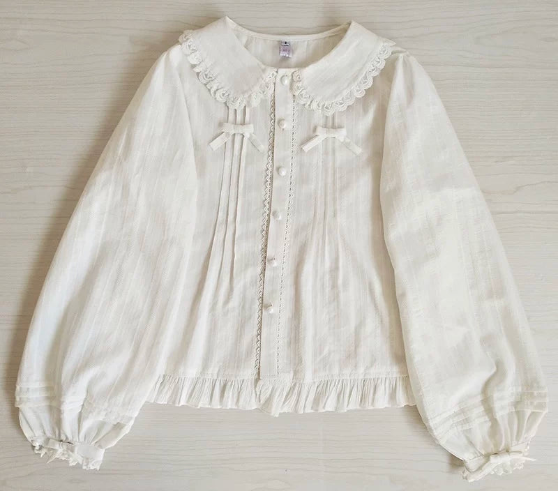 White long-sleeve inner shirt laid flat, showing its lace collar, front pleats, ribbon bows and ruffled hem.