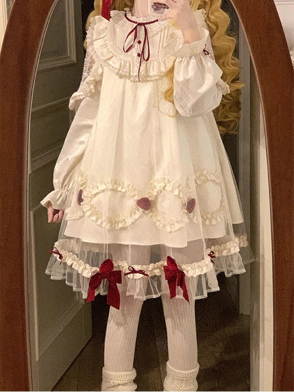 Cream long-sleeved dress with strawberry appliqués, red bows and layered ruffle trim shown in a mirror.