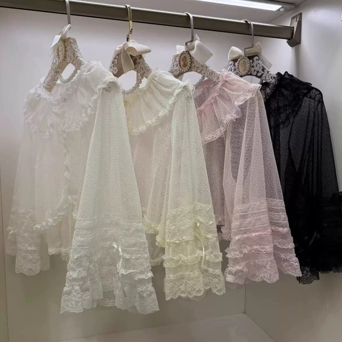 Sweetheart Dream Machine lace-trimmed blouses in white, beige, pink and black hanging on a rack.