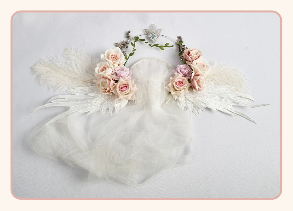 White rose crown with pink and cream roses, wing details, green vines and a sheer veil displayed flat.