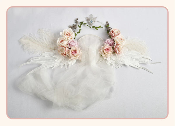 White rose crown with pink and cream roses, wing details, green vines and a sheer veil displayed flat.