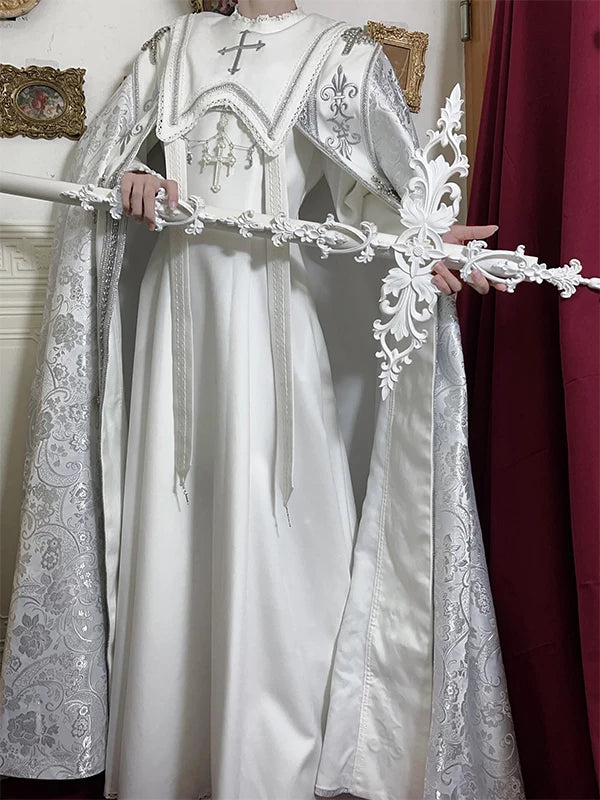 White OP dress and ornate cape with cross motifs displayed on a mannequin.