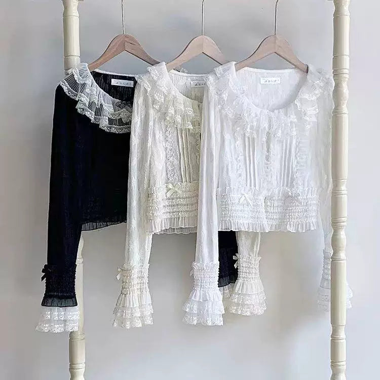White cropped cardigan with a lace ruffle collar, bow ties and gathered sleeves laid on a round woven mat.