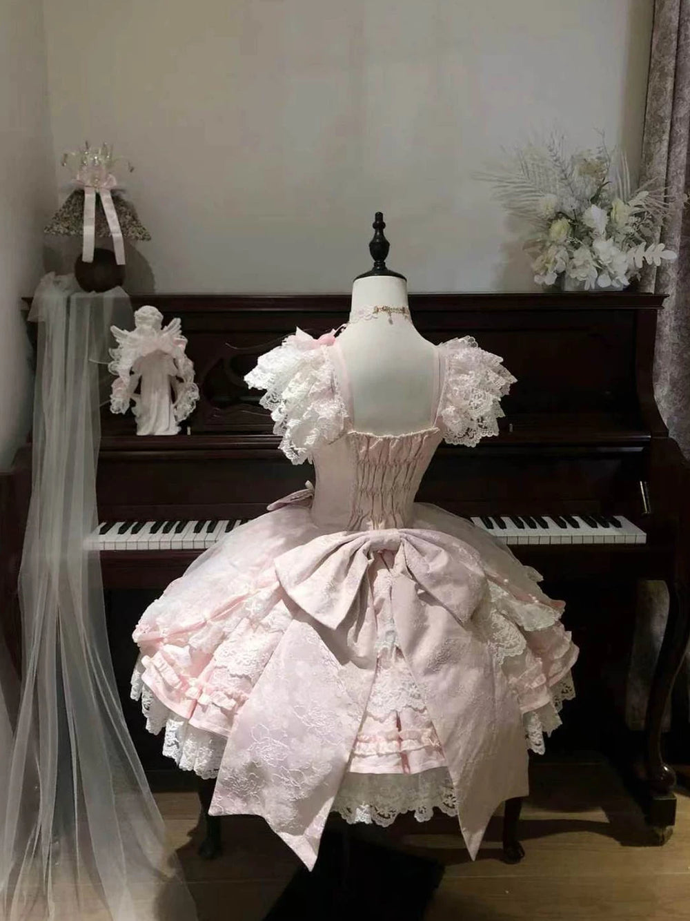 Pink lace-trimmed Lolita dress on a mannequin with a layered skirt and ribbon bows.