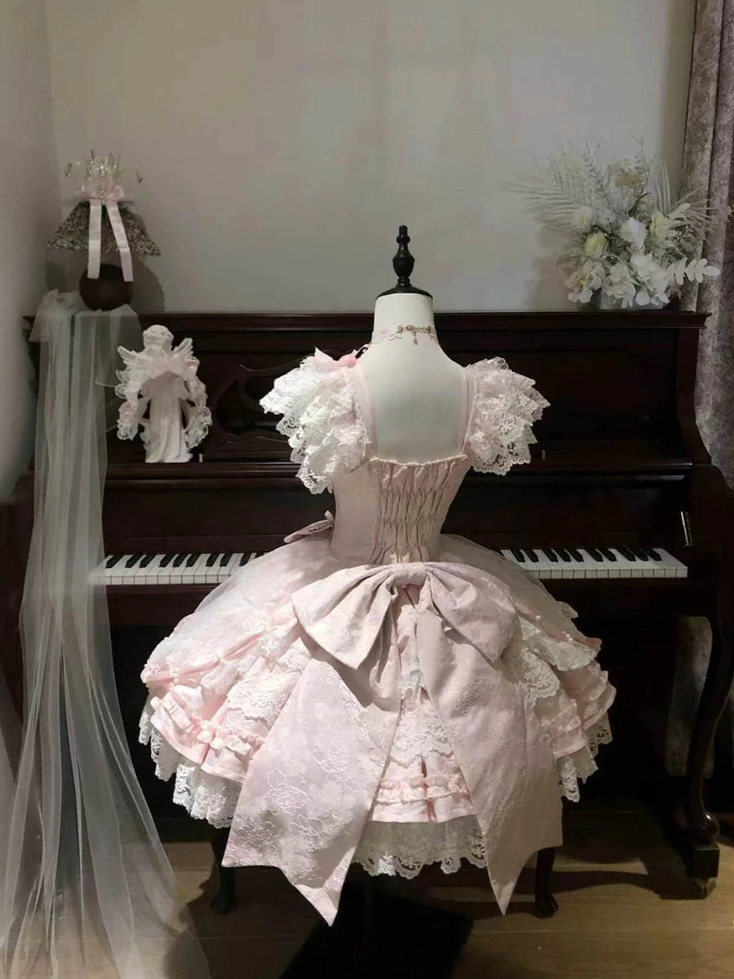 Pink lace-trimmed Lolita dress on a mannequin with a layered skirt and ribbon bows.