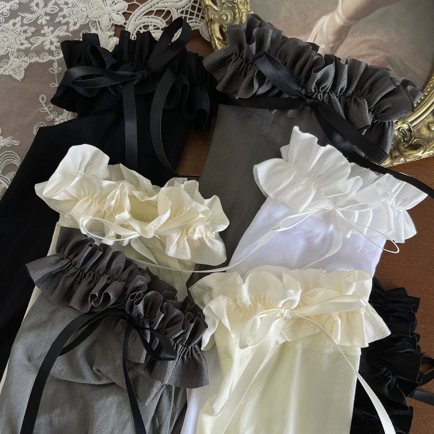 Black, gray, white and apricot ruffled bow-cuff socks arranged in a flat lay.