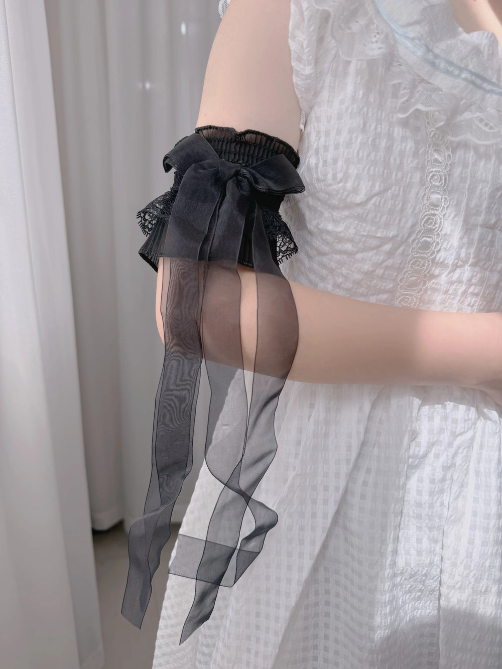 White lace-trimmed arm sleeves with long ribbon bows shown on a hand