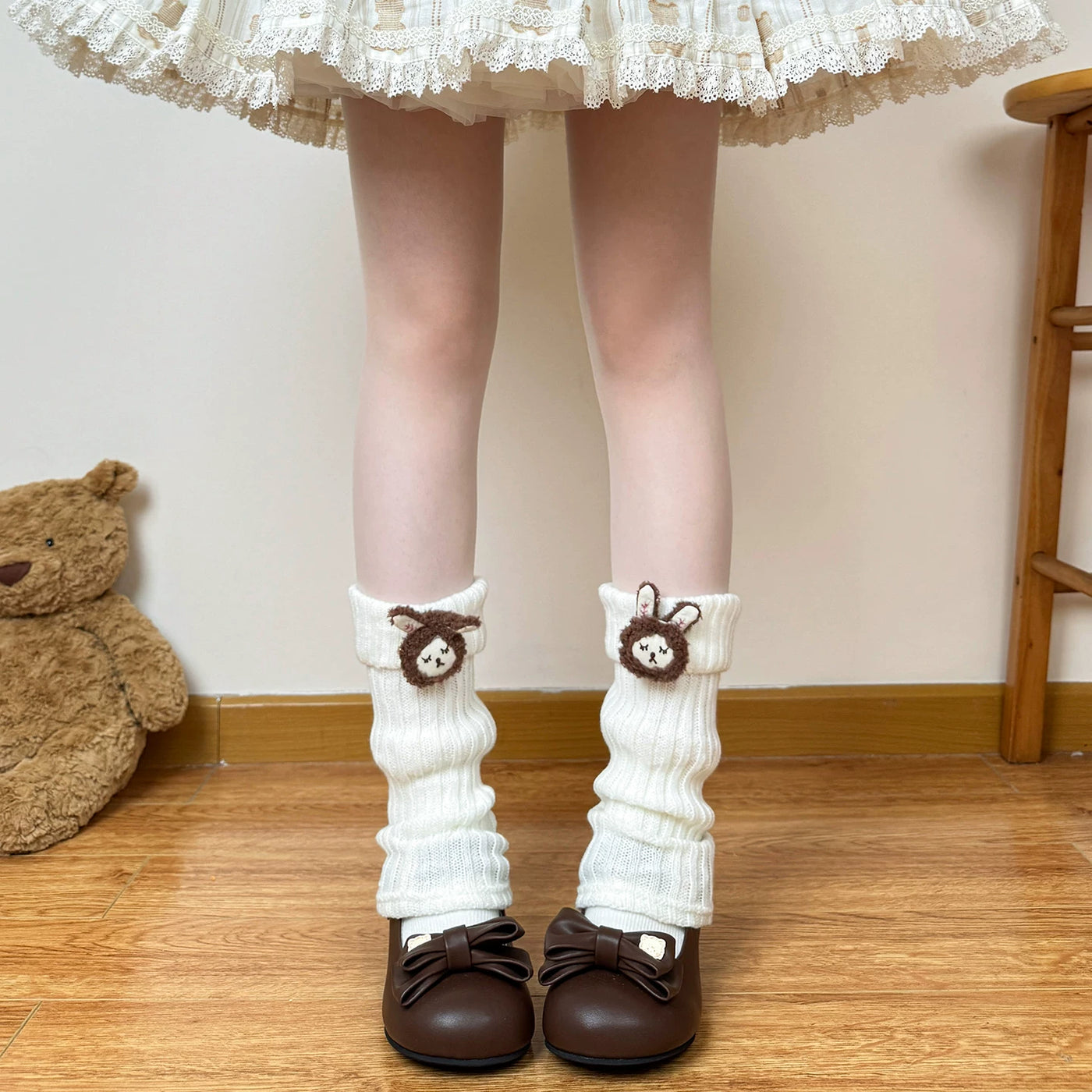 Off-white teddy-bear cuff leg warmers shown with a lace-trimmed skirt and brown shoes.