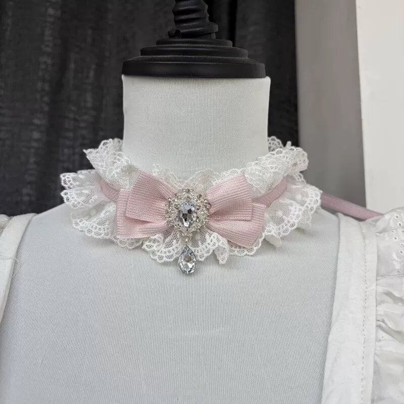 Pink lace collar necklace with a centred bow and faceted drop ornament on a mannequin.
