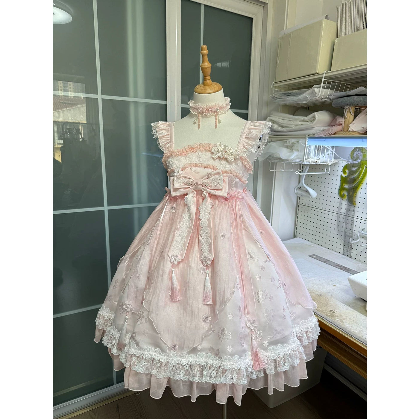 Pink high-waisted JSK dress on a mannequin with floral lace, ruffles, bows, and tassel ties
