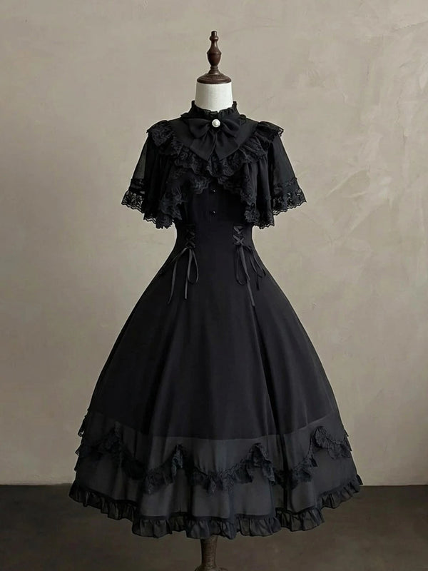 Black one-piece dress with a bow collar and layered lace cape displayed on a dress form.
