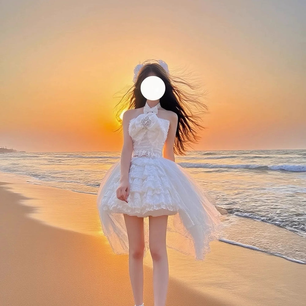 White two-piece dress set with a bow-front halter top and trailing layered skirt on a beach at sunset.