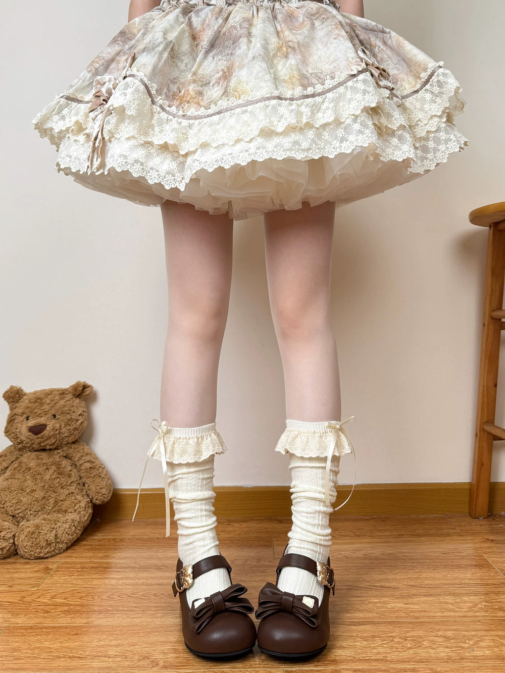 Off-white calf socks with stacked lace ruffles and ribbon ties styled with a skirt and brown shoes.