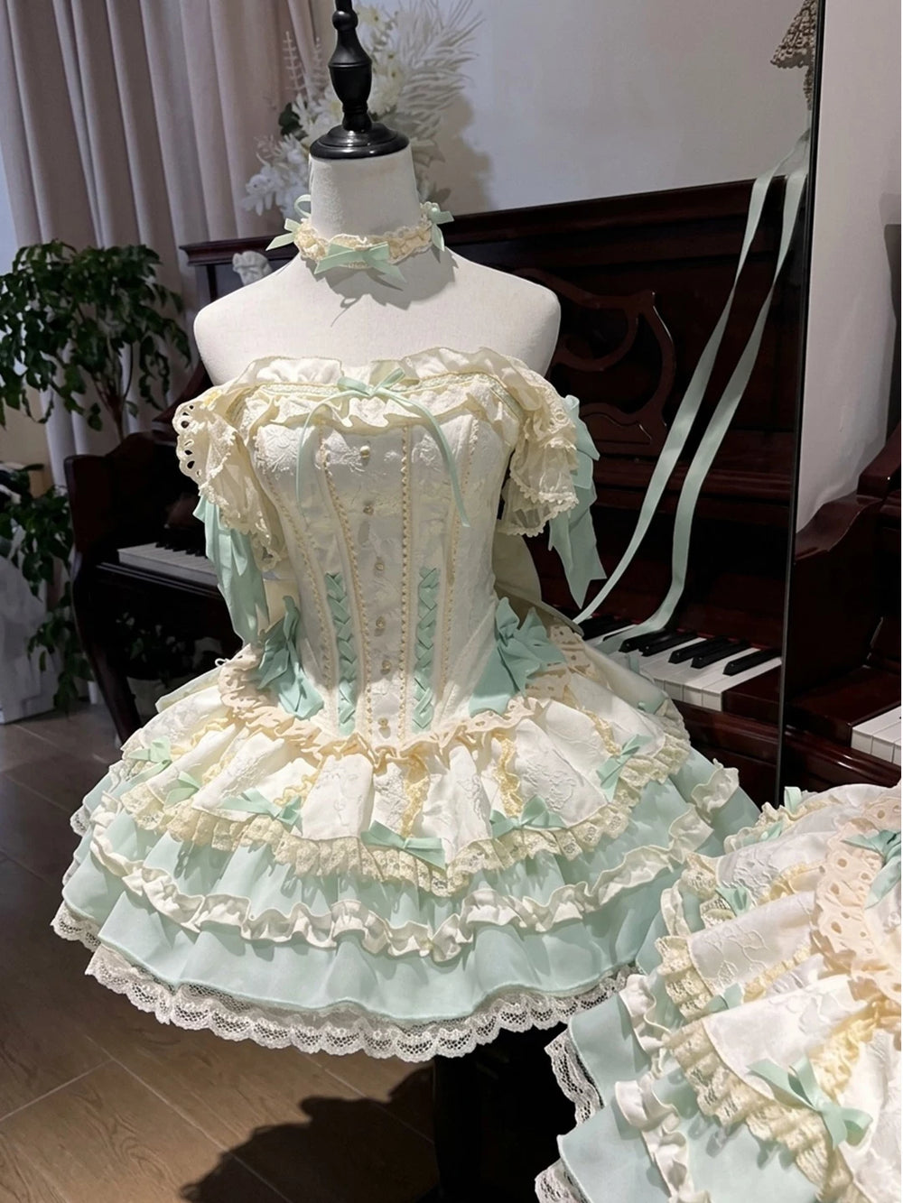 Mint-green and ivory Lolita dress with layered ruffles, bows, lace trim, train and neckpiece on a mannequin