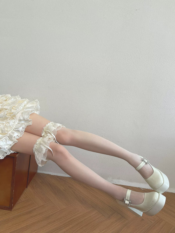 White over-the-knee socks with layered ruffles and scalloped lace edging worn with white platform shoes.