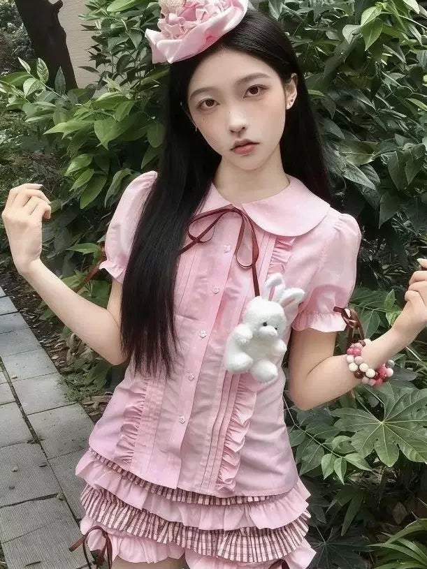 Model wearing a pink or white fitted blouse with a Peter Pan collar, ruffled front and puffed sleeves.