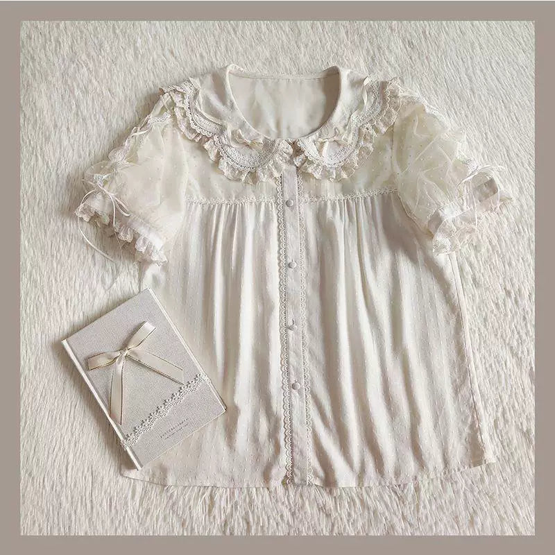 Off-white blouse with short puff sleeves, doll collar and lace edging laid flat.