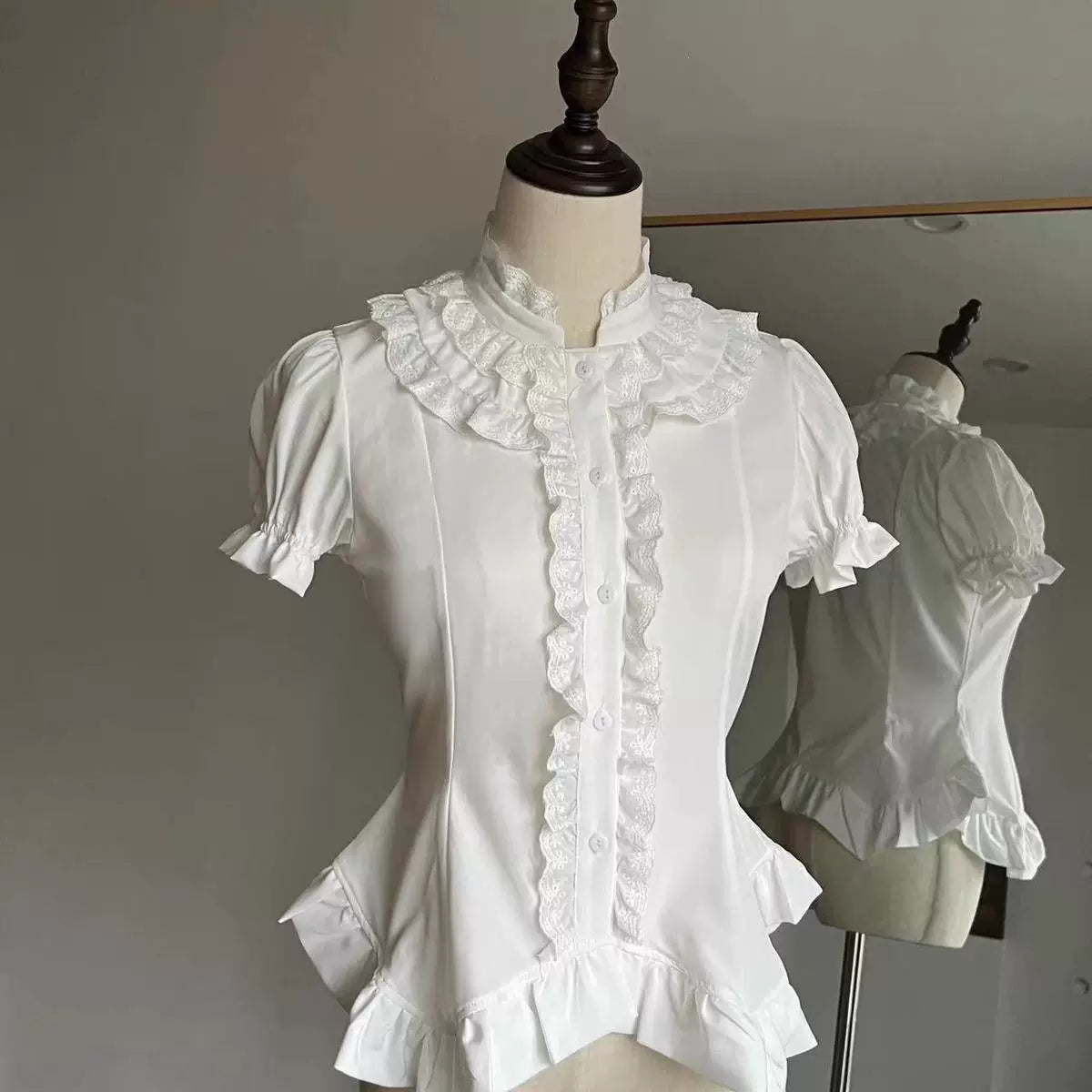 Black and white short-sleeve blouses with ruffled collars and front trim on hangers