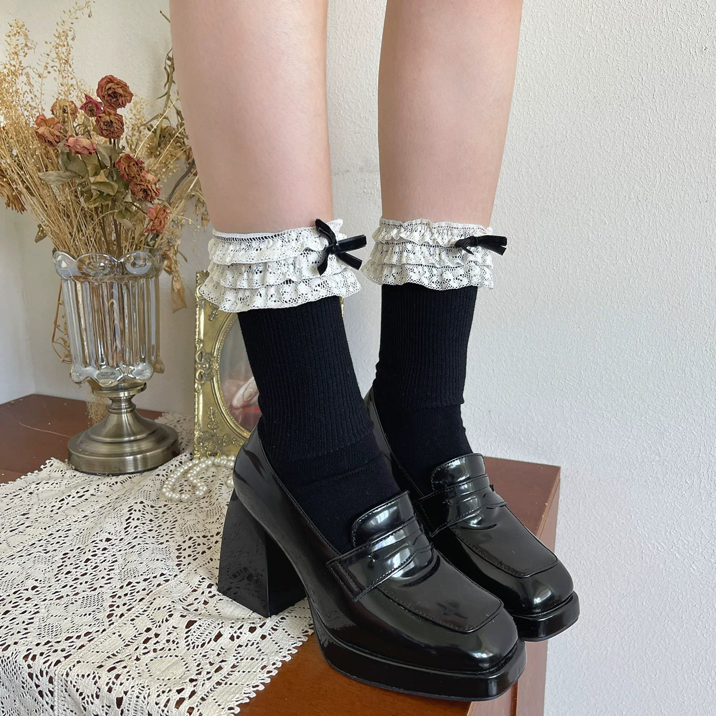 White lace-trimmed scrunched socks with tiered cuffs styled with cream Mary Jane shoes.