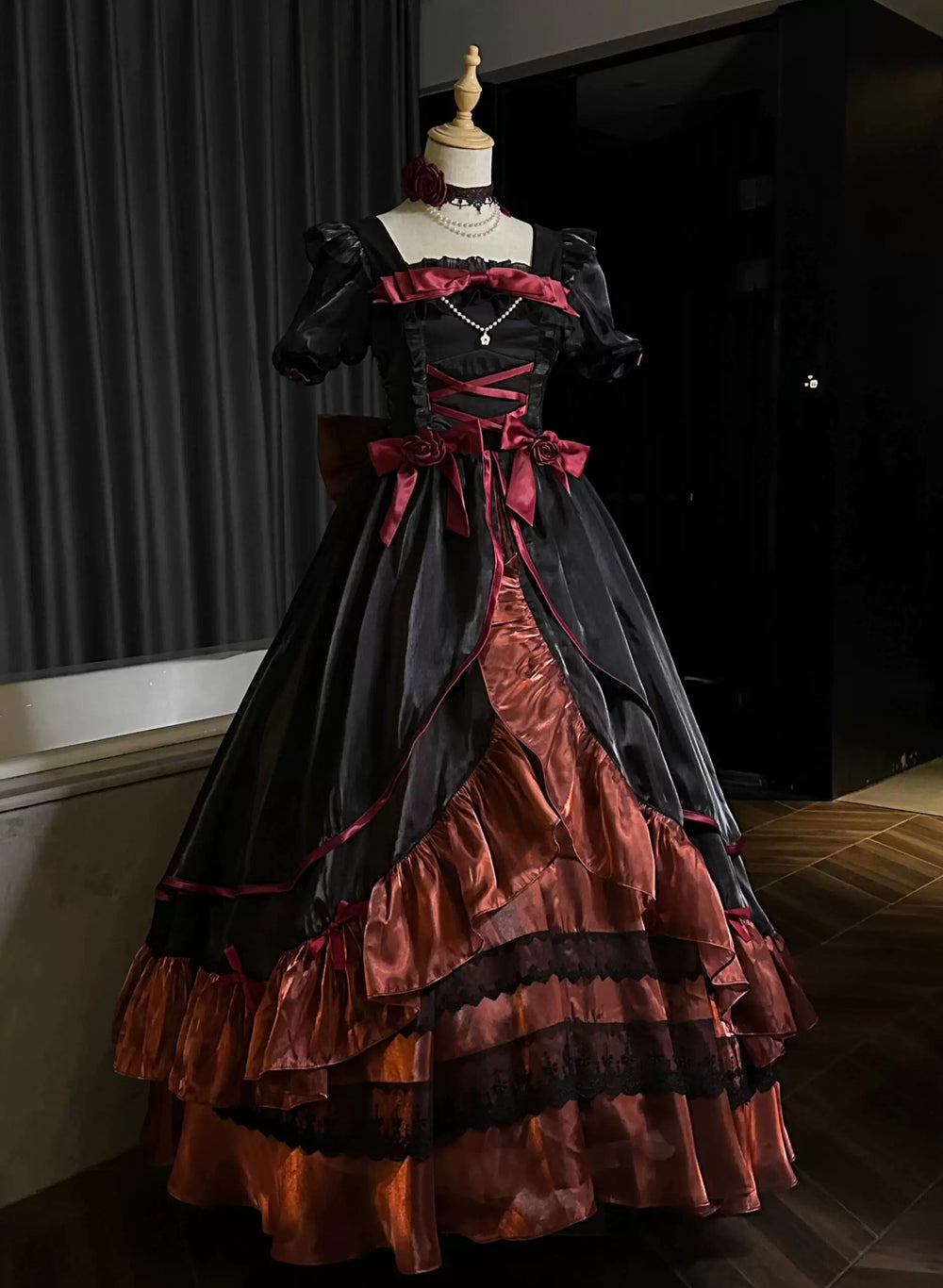 Black-and-deep-red one-piece dress with rose accents, bows, layered ruffles, and a train on a mannequin.
