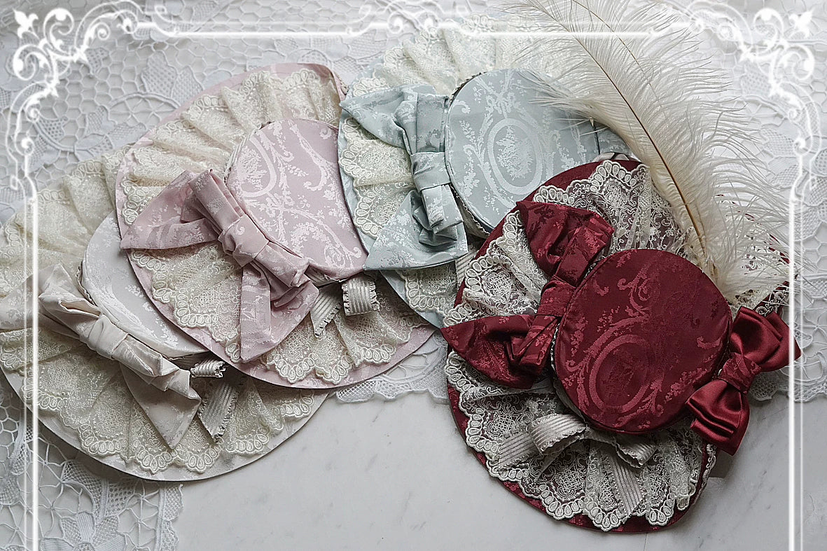 Mary's Portrait headwear with lace, ribbon bows, feather trim and ornate printed fabric.