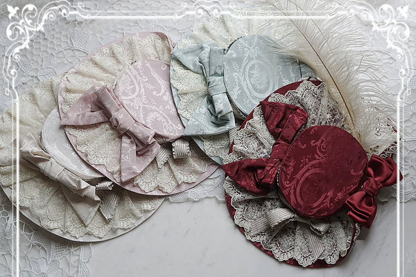 Mary's Portrait headwear with lace, ribbon bows, feather trim and ornate printed fabric.