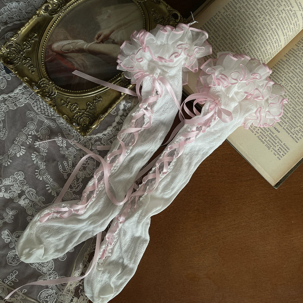White lace socks with pink ribbon straps shown in a styled flat lay