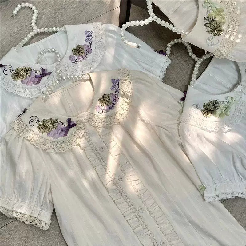 Several off-white blouses with grape embroidery, lace collars and bow accents arranged together.
