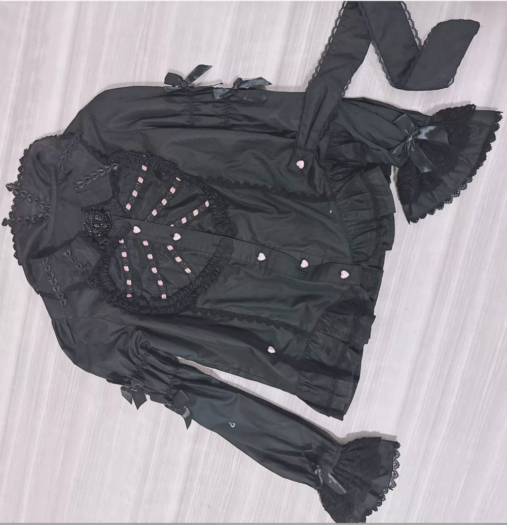 Black long-sleeve blouse with heart panel, lace trim and ribbon ties arranged flat.