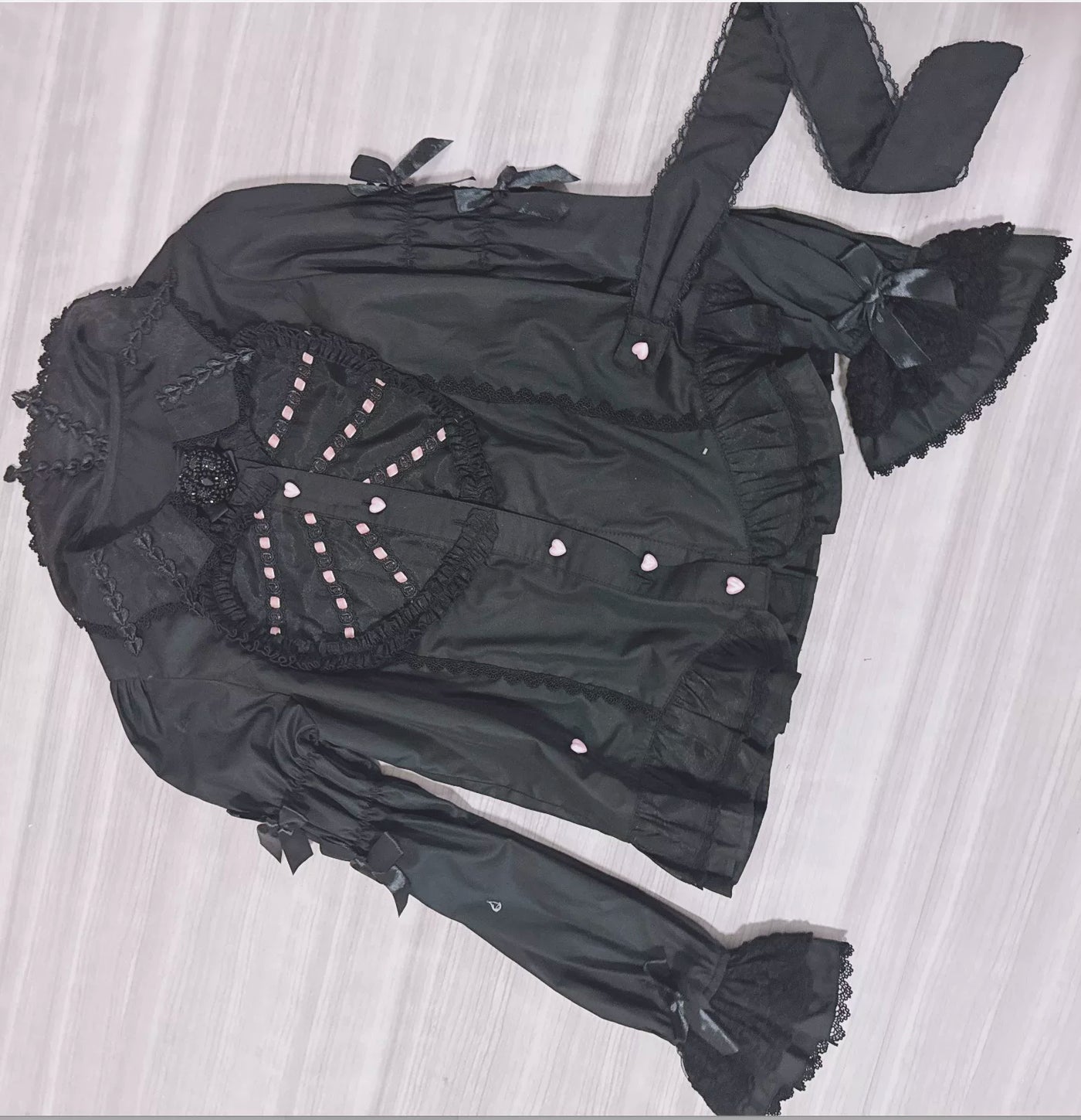 Black long-sleeve blouse with heart panel, lace trim and ribbon ties arranged flat.