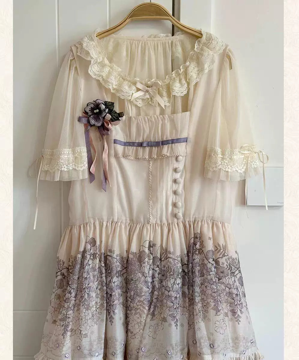 White chiffon cardigan with a ruffled lace collar, mesh sleeves and a floral chest brooch on a hanger.